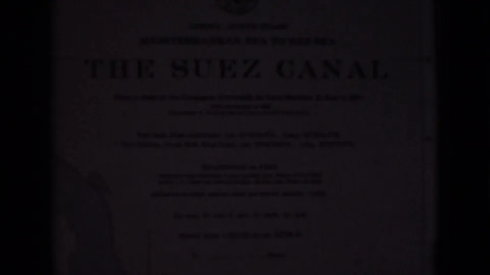 Soft, dark 1946 8mm frame showing a Suez Canal plaque in Egypt with a large printed title, small text, and partial map outline.