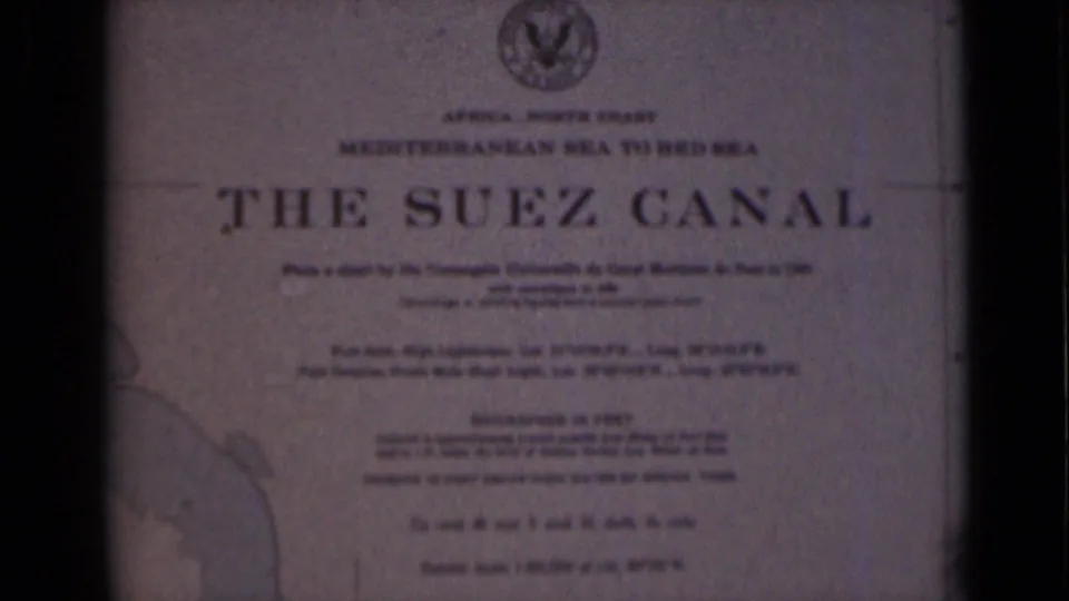 1946 8mm frame of the Suez Canal plaque in Egypt, framed by dark borders and showing the title, emblem, text, and partial map.