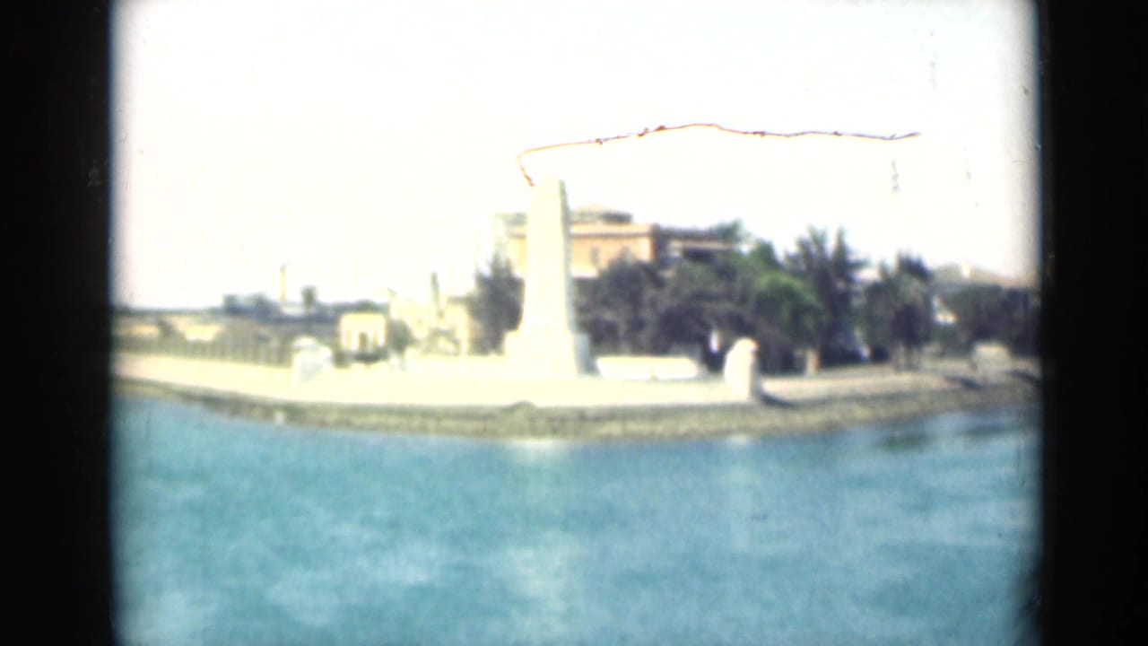 Boat-level view of a white waterfront monument beside blue canal water.