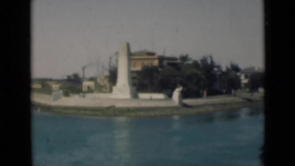 1946 8mm view along the Suez Canal showing calm water, a white monument, and low shoreline buildings in Egypt.