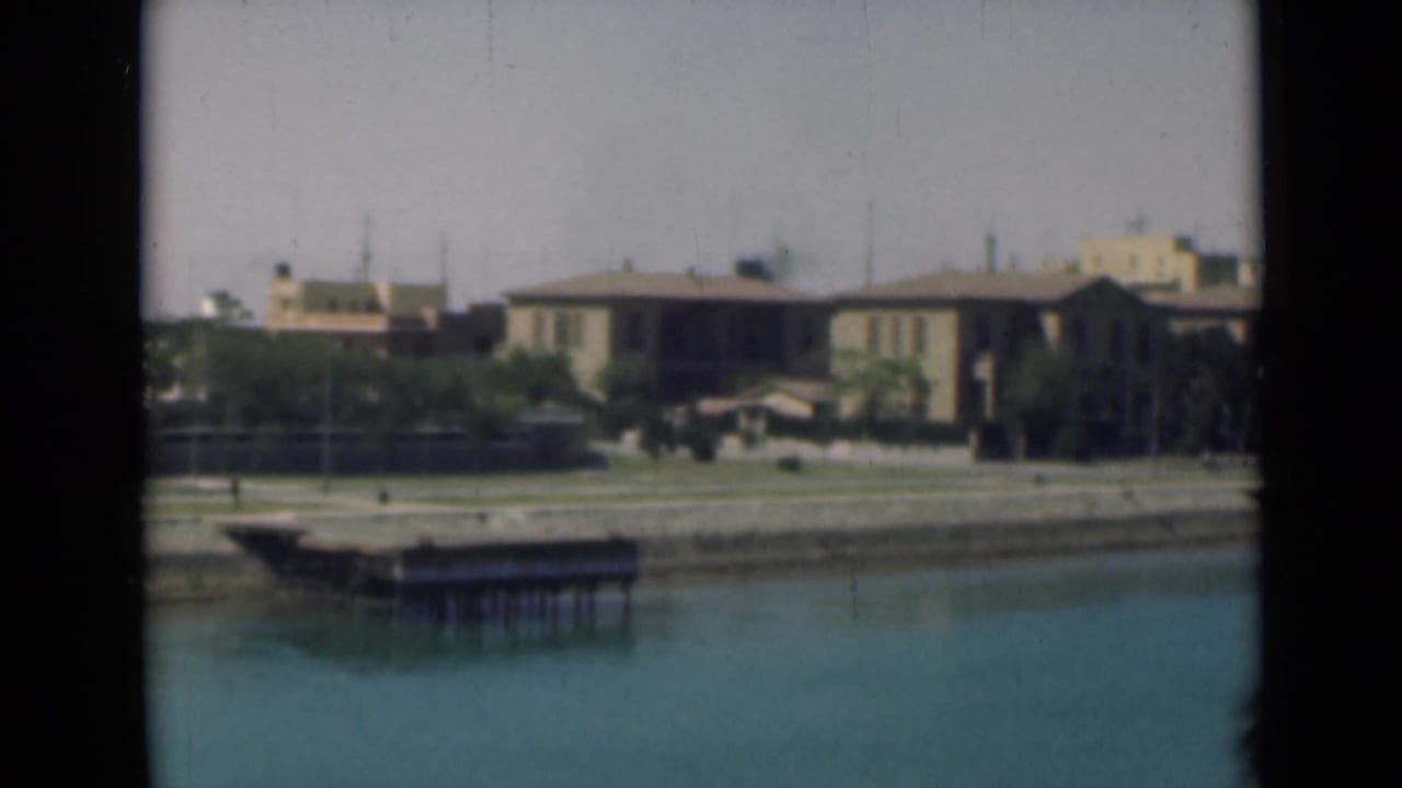 1946 Egypt canal-side frame showing a small dock, still water, low houses, and shoreline planting.