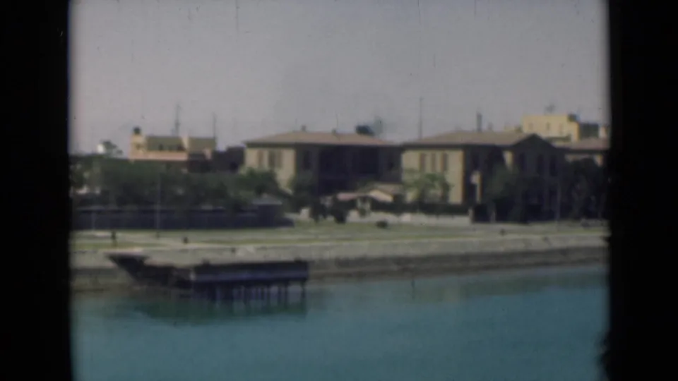 1946 Egypt canal-side frame showing a small dock, still water, low houses, and shoreline planting.