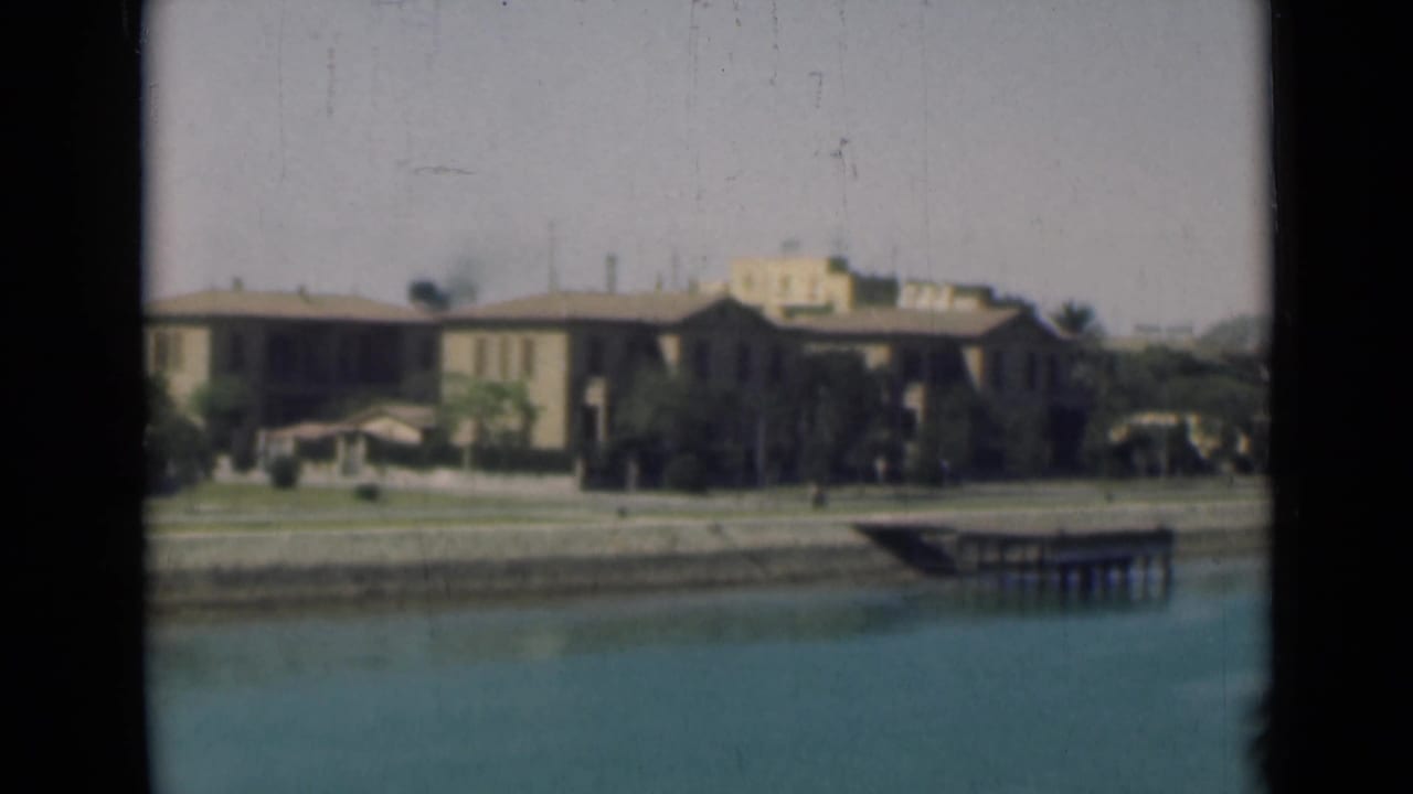 Low buildings, shoreline, dock, and canal water framed by dark vertical edges.