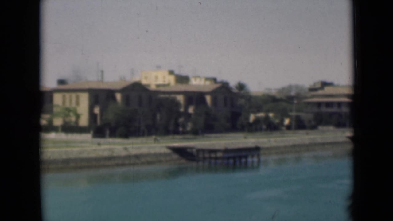 1946 Suez Canal waterfront showing low buildings, palms, a sloped embankment, and dock structures.