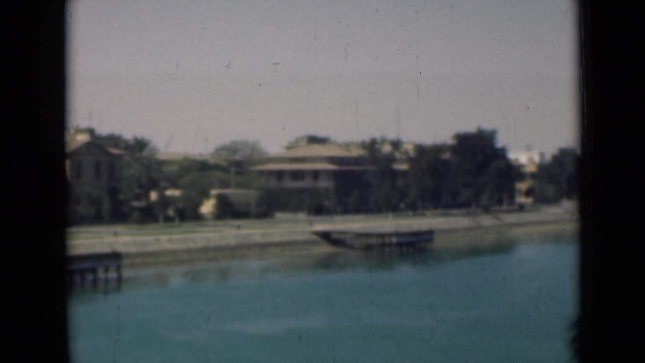 Suez Canal waterfront in 1946, showing blue water, low tan buildings, trees, and a small dock under clear daylight.
