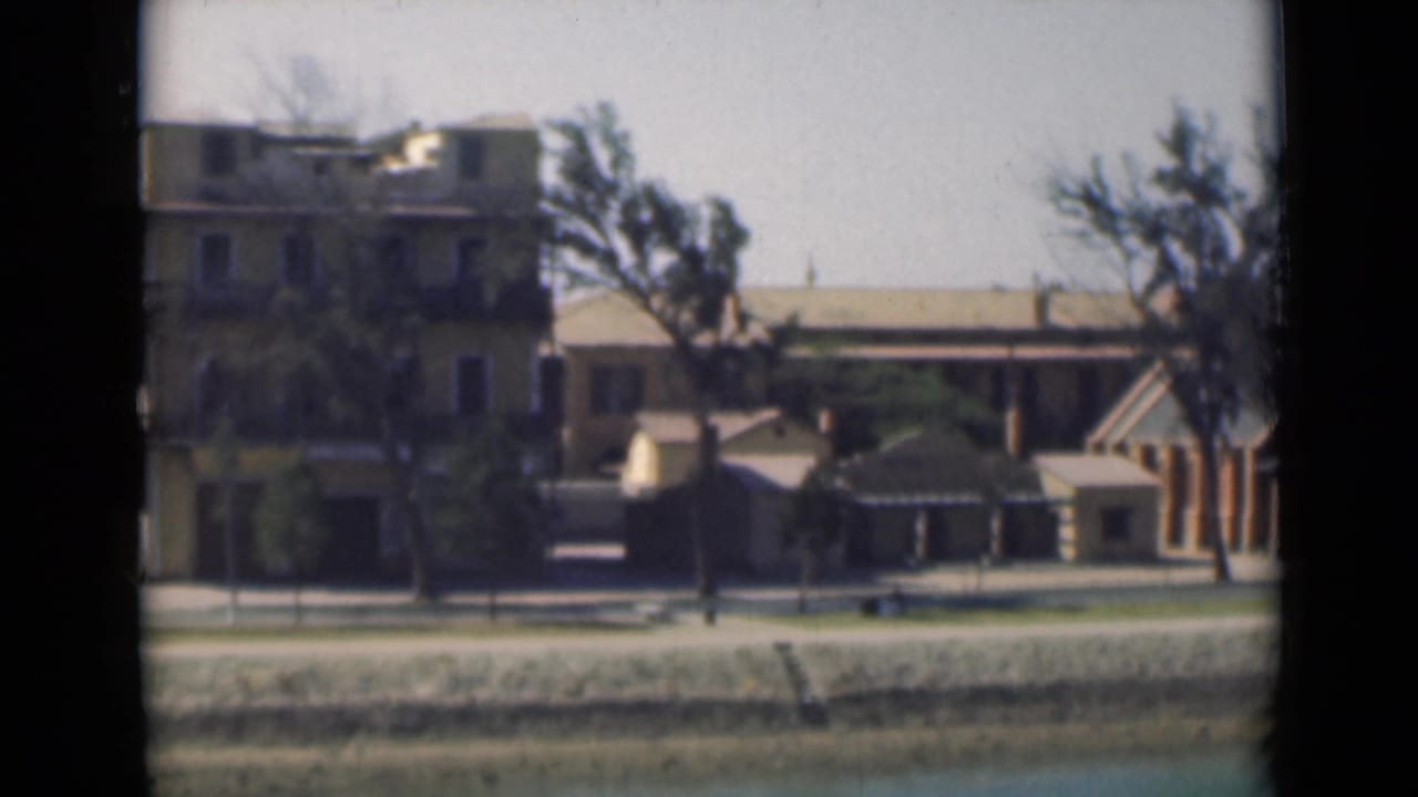 Suez Canal bank in 1946 with a tan building, trees, paved waterfront, and calm water, framed by visible 8mm film borders.