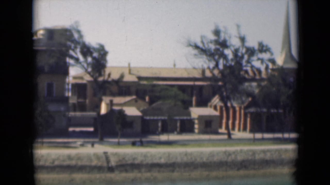 1946 Suez Canal view with canal bank, low buildings, trees, and a church steeple entering the right side of frame.