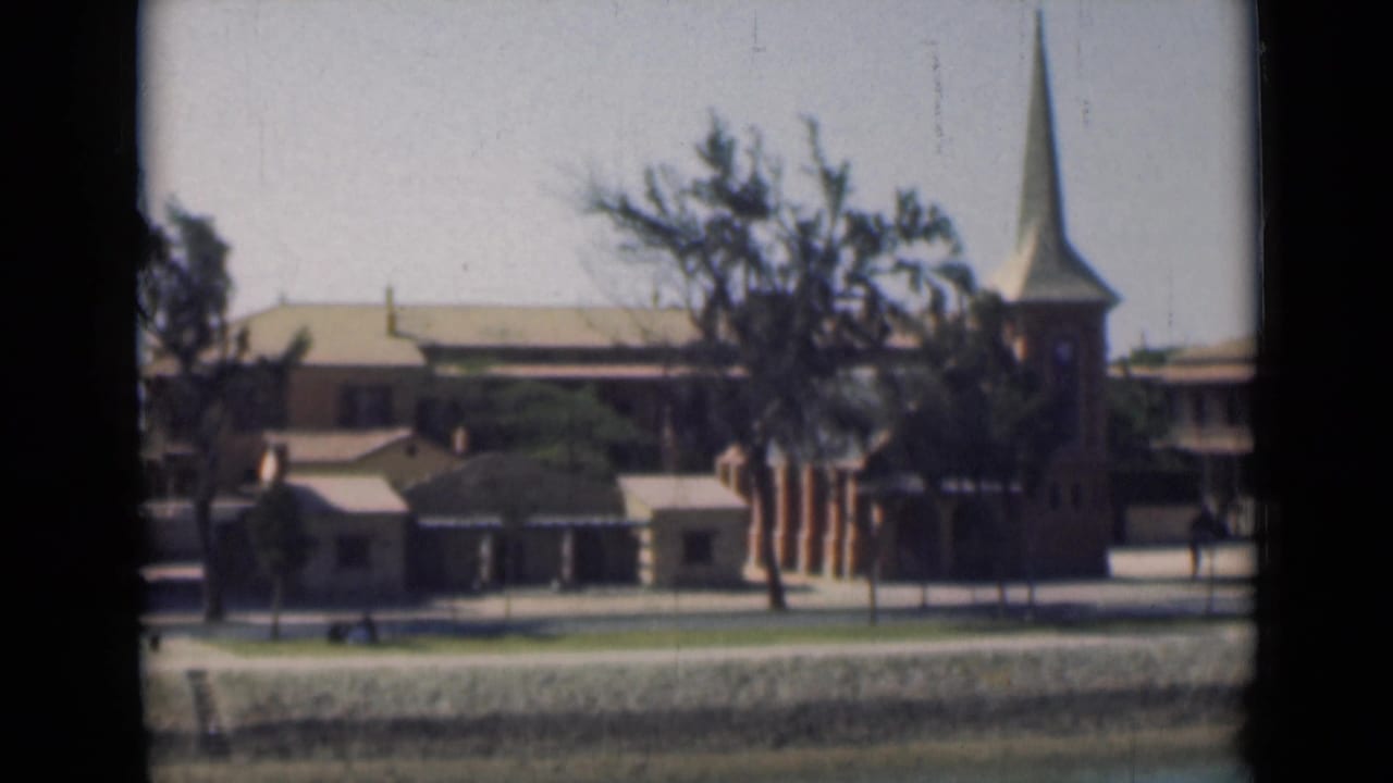 1946 Suez Canal waterfront with a brick church tower, pointed steeple, nearby buildings, trees, and canal bank.