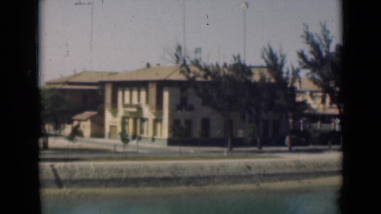 1946 Suez Canal waterfront view with a pale building, tiled roof, trees, quay wall, and calm water in the foreground.