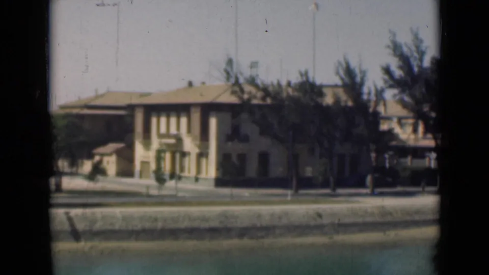 1946 Suez Canal waterfront view with a pale building, tiled roof, trees, quay wall, and calm water in the foreground.