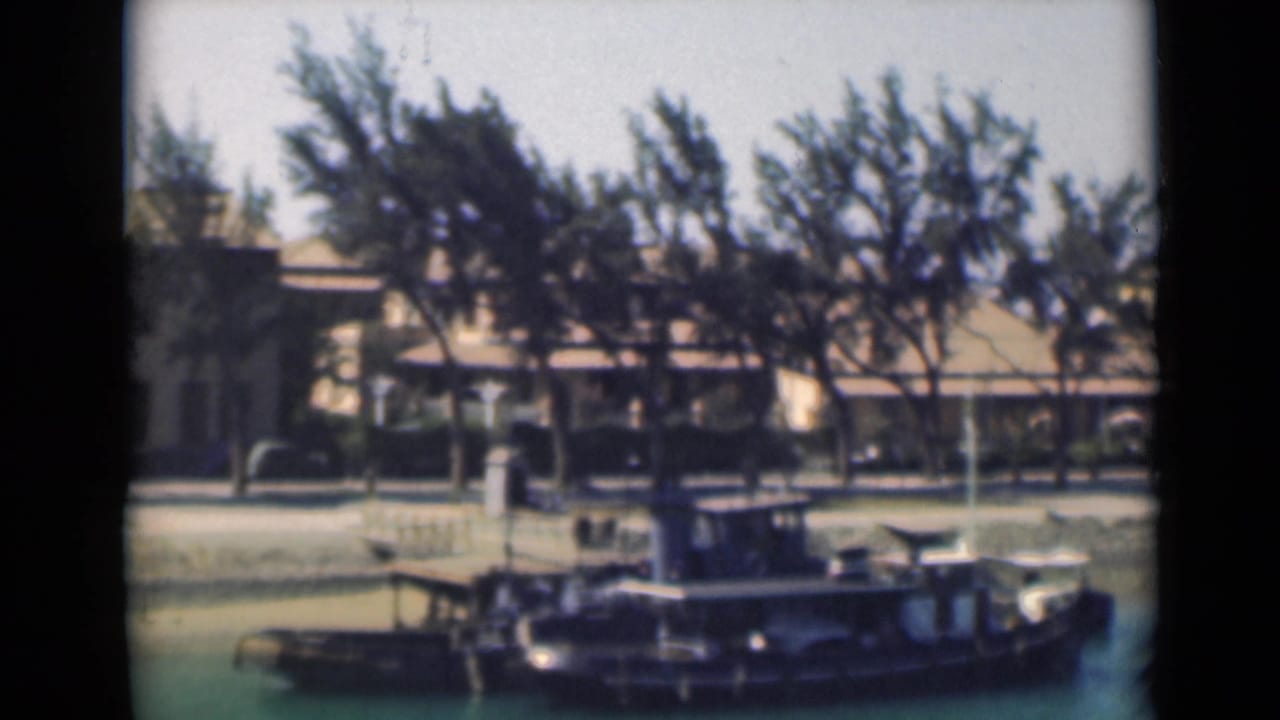 1946 Suez Canal home-movie frame showing a small vessel near a tree-lined bank and low waterfront building.