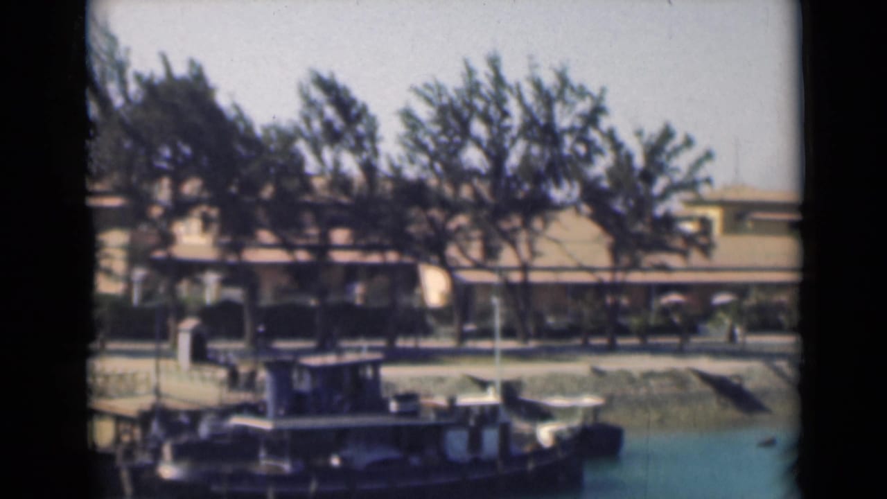 A 1946 Suez Canal view from 8mm footage, with a small vessel in the foreground and a tree-lined waterfront behind it.