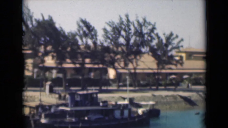 A 1946 Suez Canal view from 8mm footage, with a small vessel in the foreground and a tree-lined waterfront behind it.