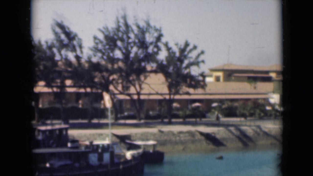 Soft 8mm view of the Suez Canal in 1946, with part of a boat, canal water, trees and a low shoreline building.
