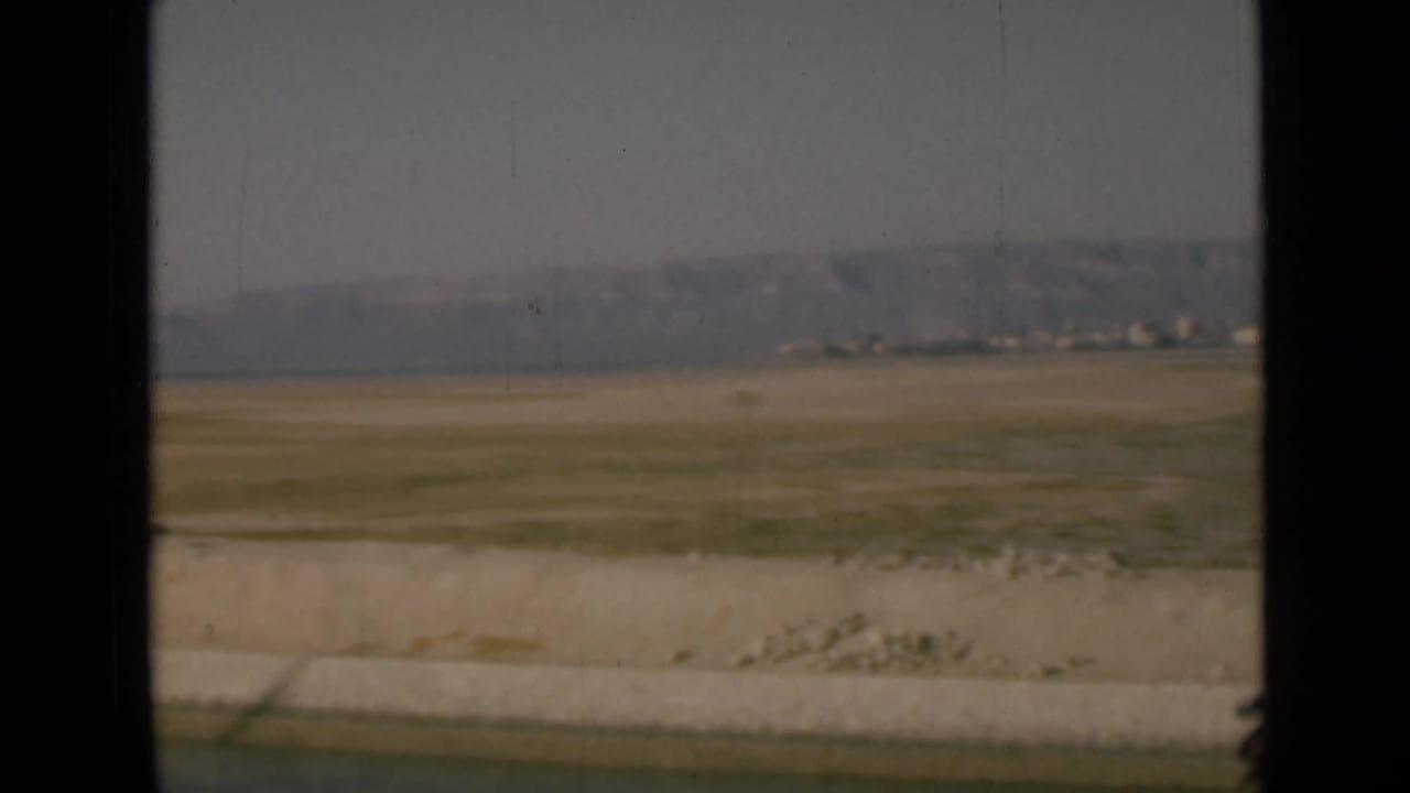 1946 Suez Canal area view with a pale embankment, open desert flats, distant hills, and small indistinct structures near the horizon.