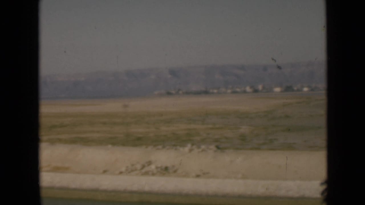 1946 8mm view in the Suez Canal region showing flat desert ground, distant settlement traces, hazy hills, and a foreground road edge.