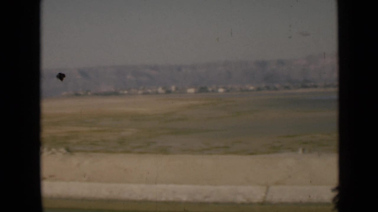 1946 Suez Canal region landscape with a pale sky, flat open ground, distant low structures, and hazy hills beyond the road edge.