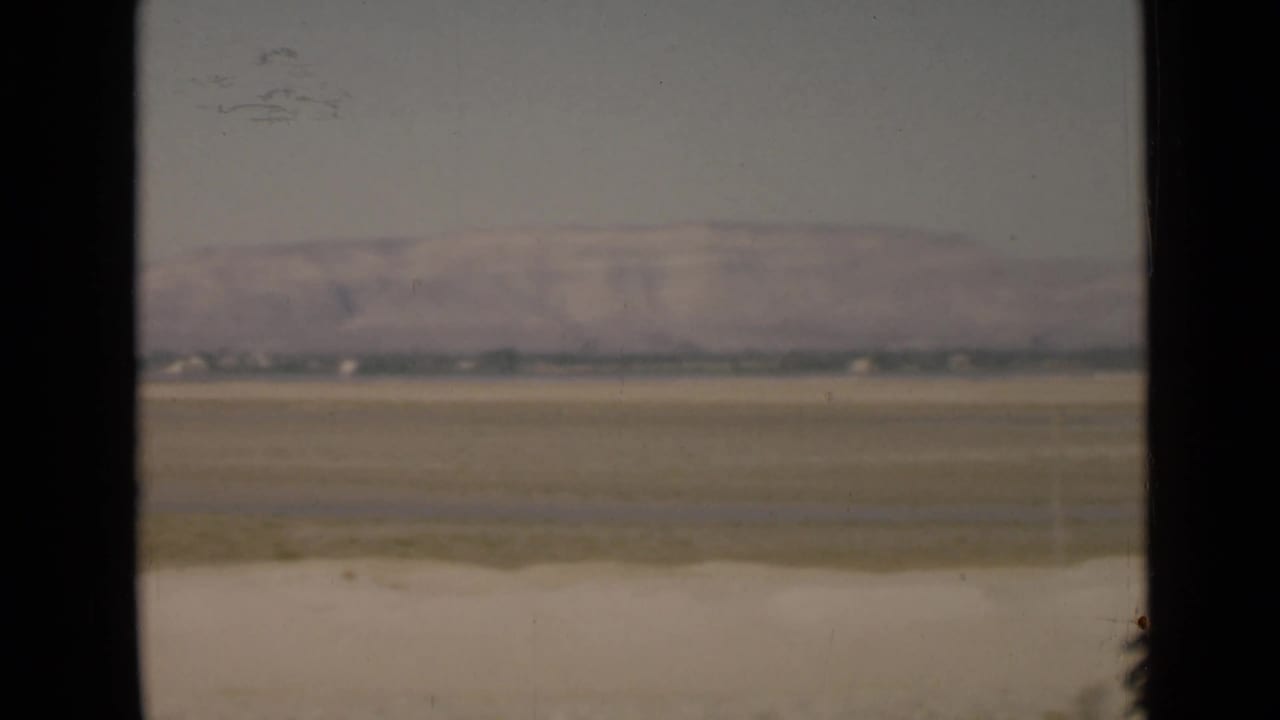 1946 8mm landscape view near the Suez Canal, with a broad flat plain, hazy mountain ridge, and pale roadside strip in the foreground.