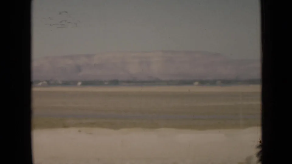 1946 8mm landscape view near the Suez Canal, with a broad flat plain, hazy mountain ridge, and pale roadside strip in the foreground.