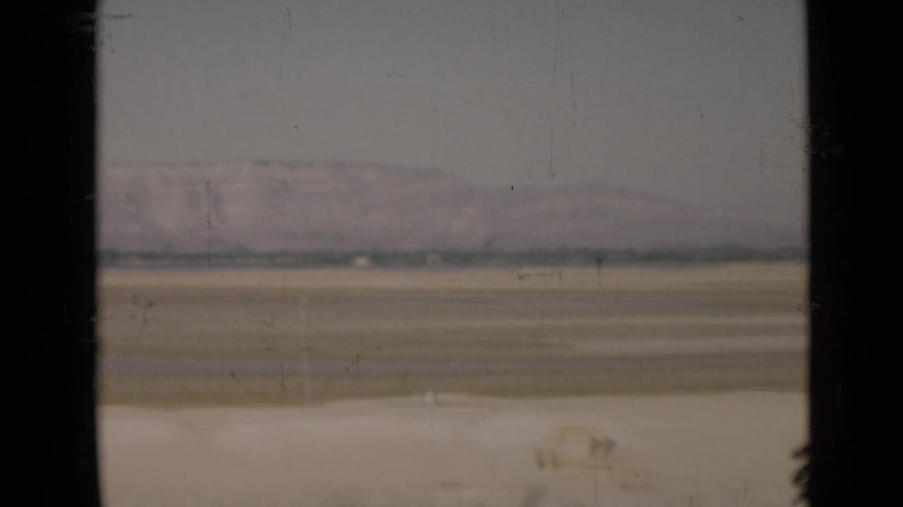 Muted 8mm view of flat sandy terrain near the Suez Canal region, framed by a dark vertical window edge.
