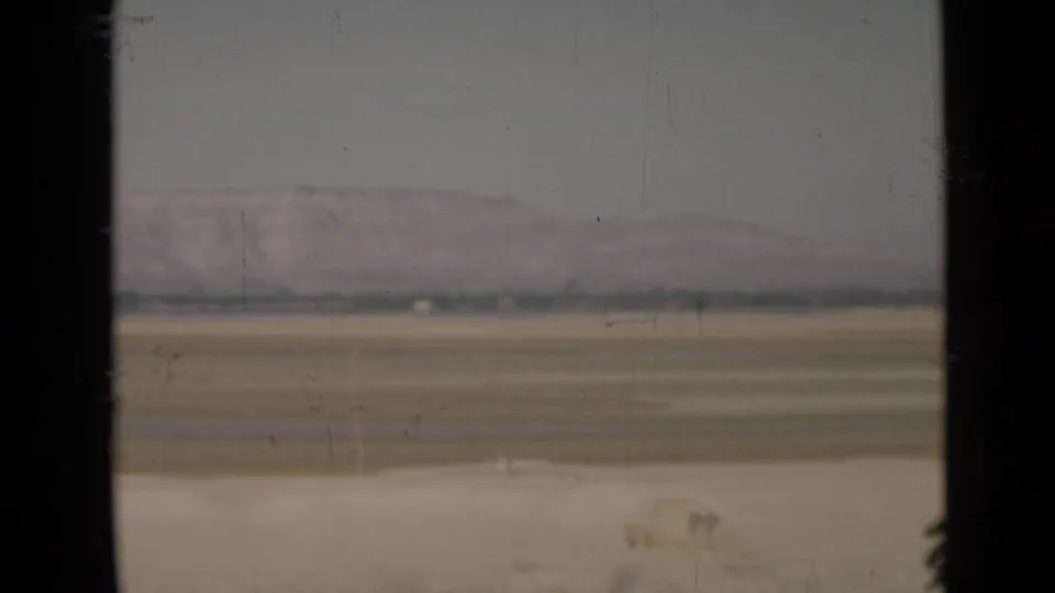 Muted 8mm view of flat sandy terrain near the Suez Canal region, framed by a dark vertical window edge.