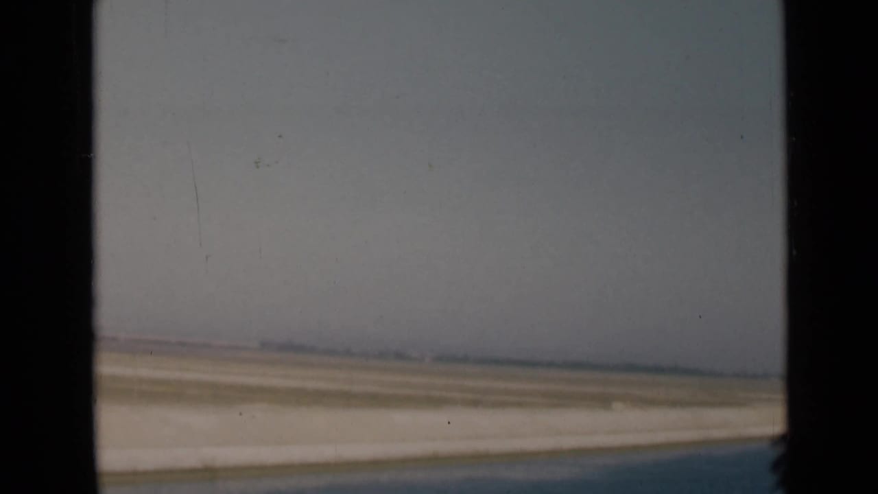 1946 canal-region view with pale shoreline, flat desert, blue water, and a dark window edge in the foreground.