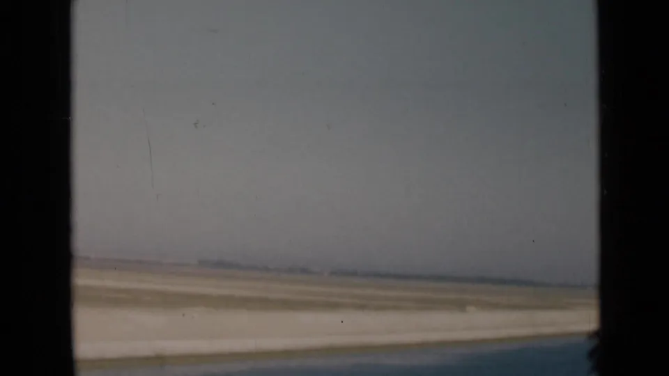 1946 canal-region view with pale shoreline, flat desert, blue water, and a dark window edge in the foreground.
