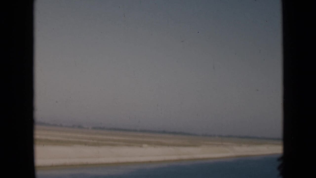 Flat sandy landscape and pale sky framed by a vehicle window.