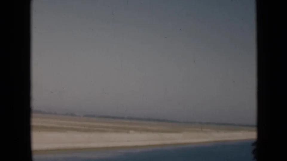 Passenger-window view near the Suez Canal area, with flat desert ground, pale sky, and a distant low horizon.