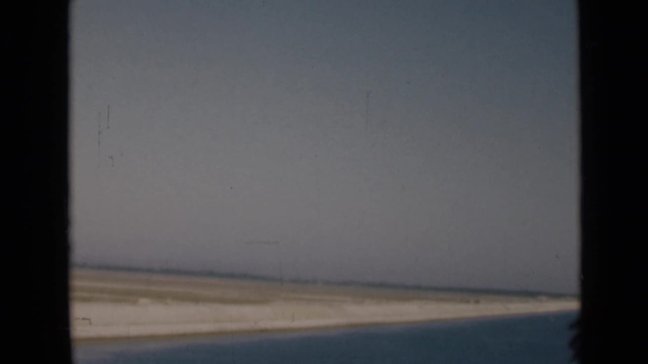 Suez Canal area travel view with pale desert, a low horizon, and a dark blue foreground edge framed by the vehicle window.