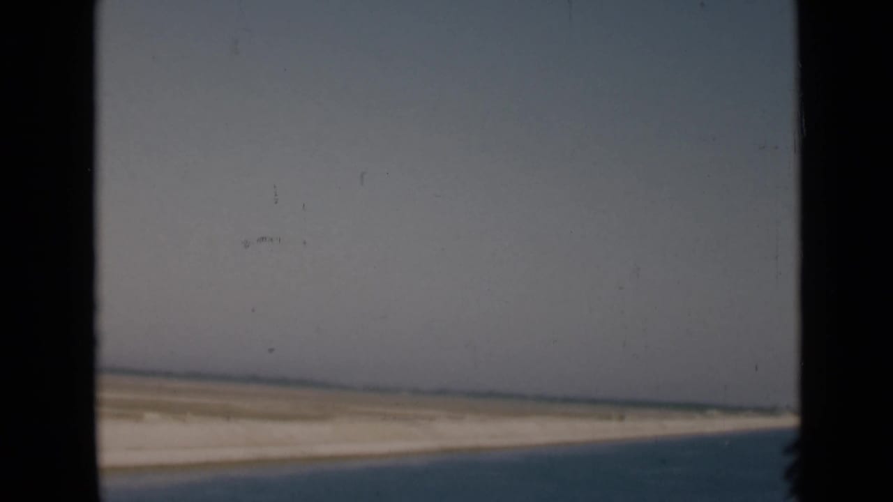 Canal water and sandy shoreline seen through dark vertical framing.