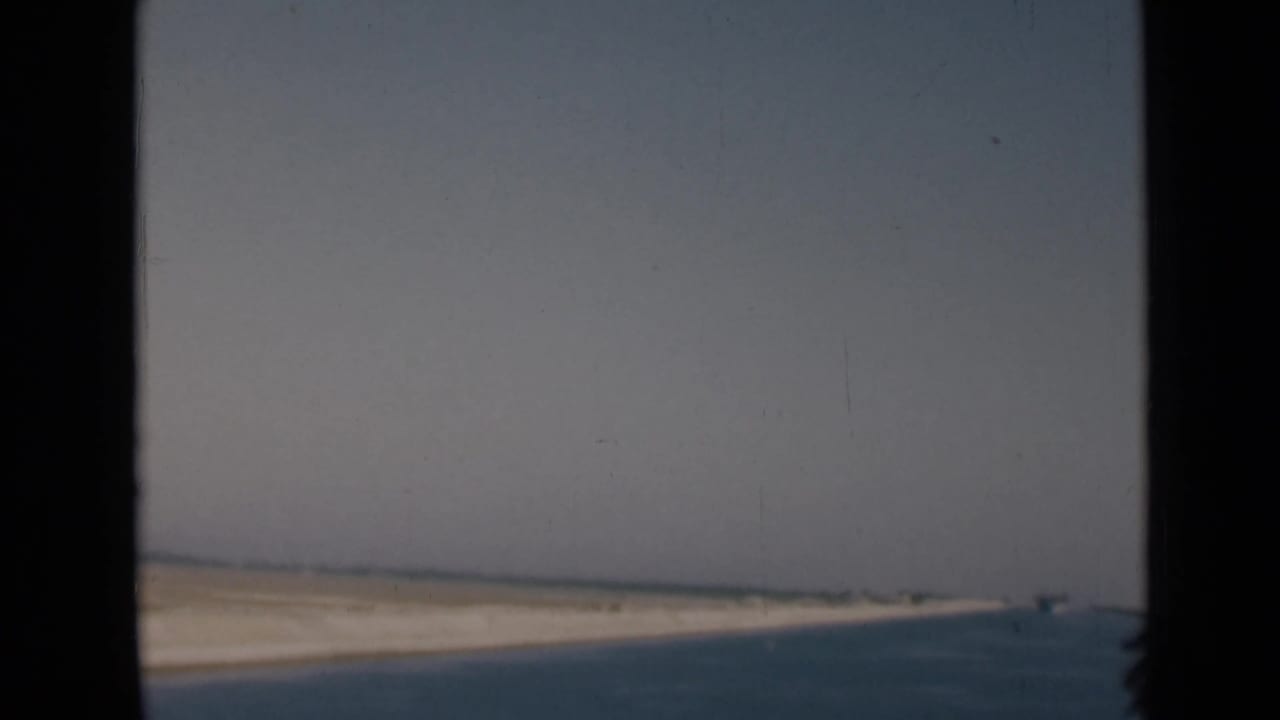 Soft 8mm frame of the Suez Canal, with open water, a narrow sandy shore, and a hazy horizon.