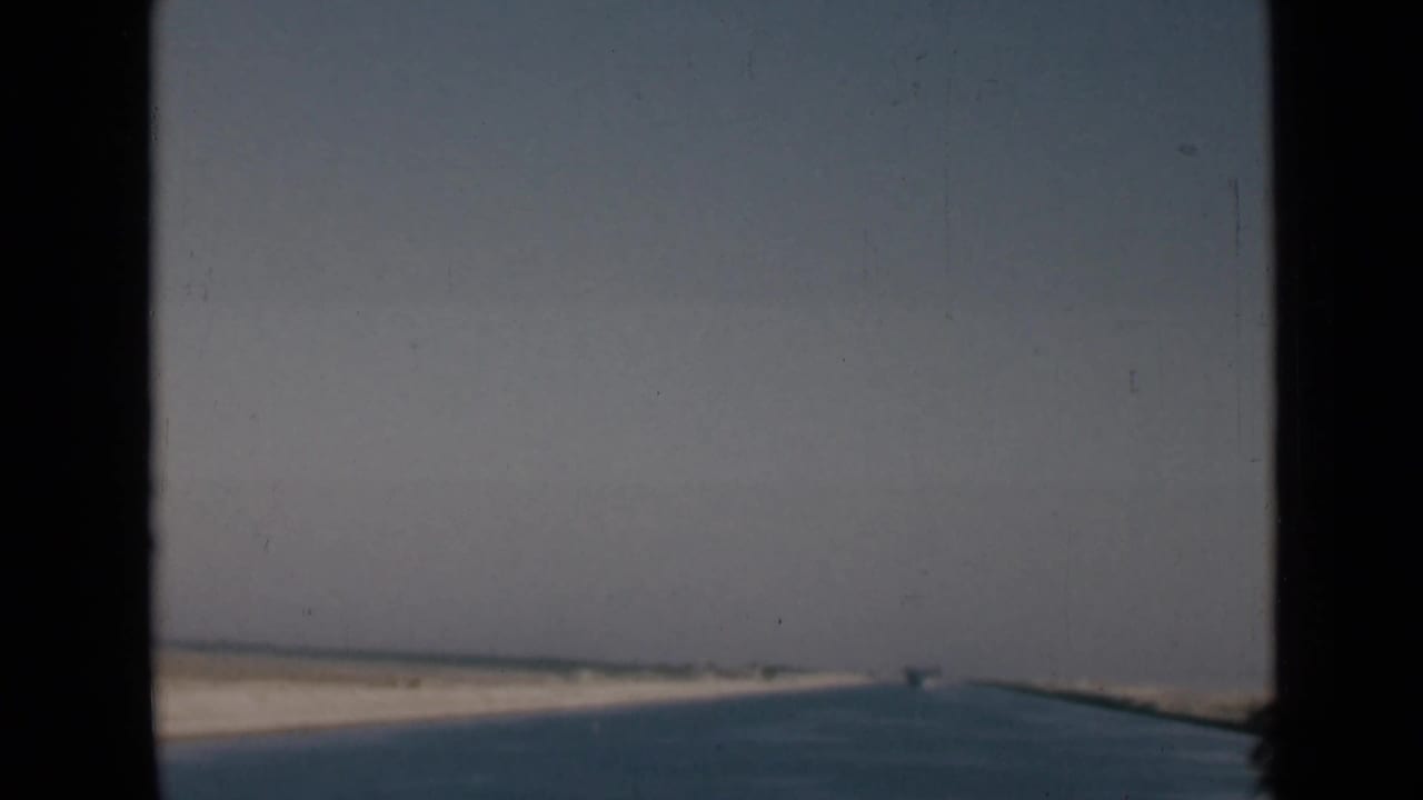 Forward-facing 1946 Suez Canal view from a vessel, with water leading toward distant sandy banks.
