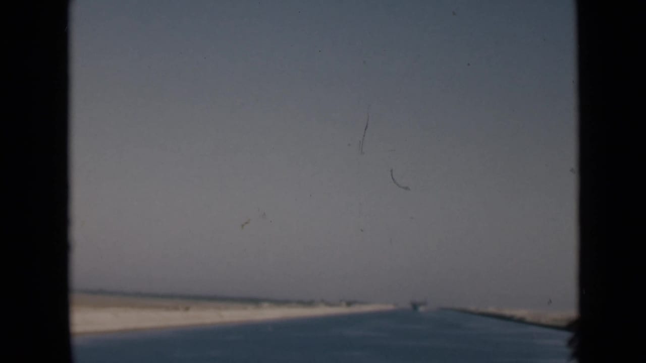 Canal water and sandy banks seen through dark ship structure.