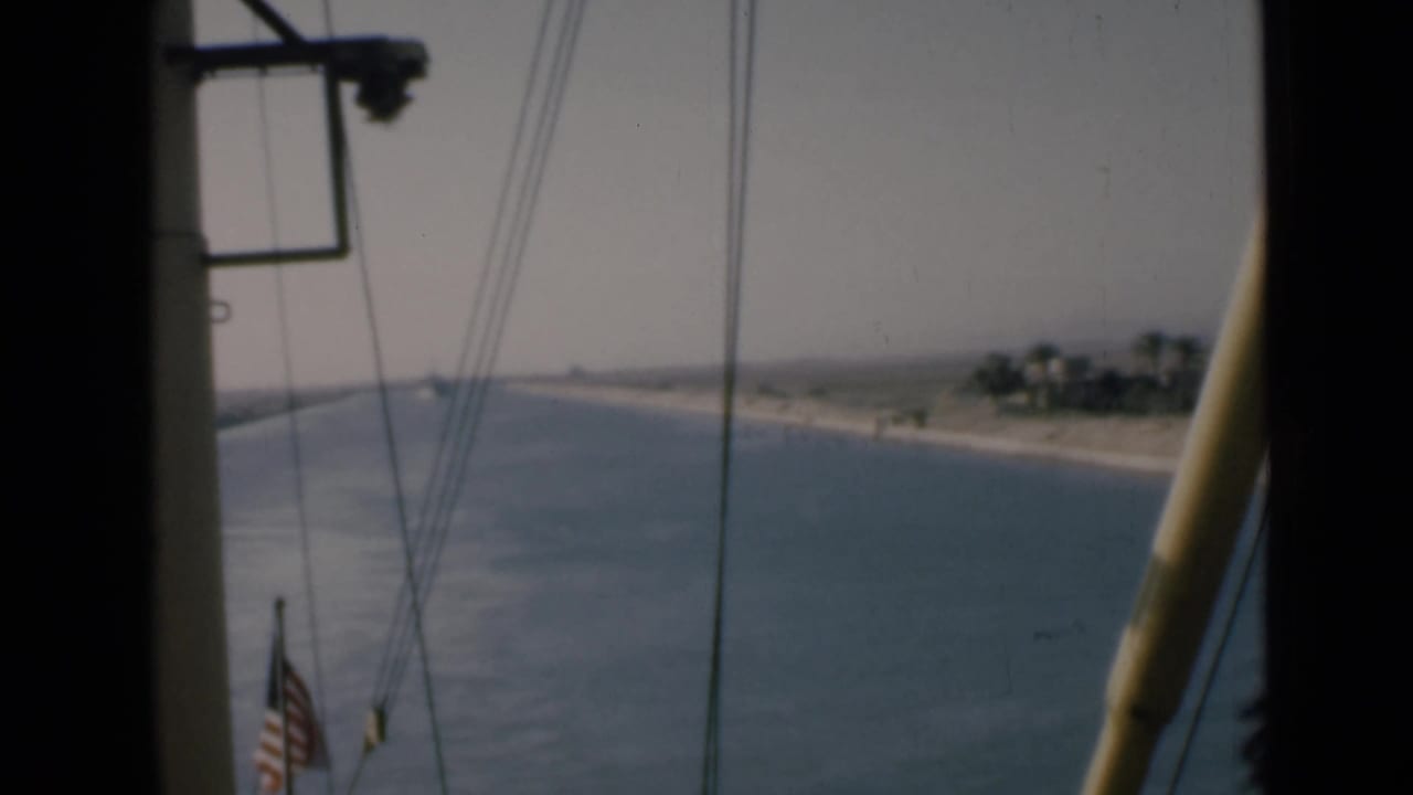 Onboard 8mm frame from the Suez Canal showing an American flag, rigging, waterway, and low Egyptian shoreline.