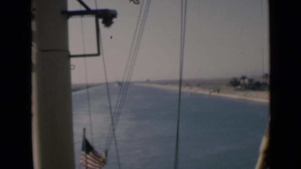 1946 Suez Canal shipboard view showing blue water, pale shore, vessel rigging, and an American flag near the lower frame.