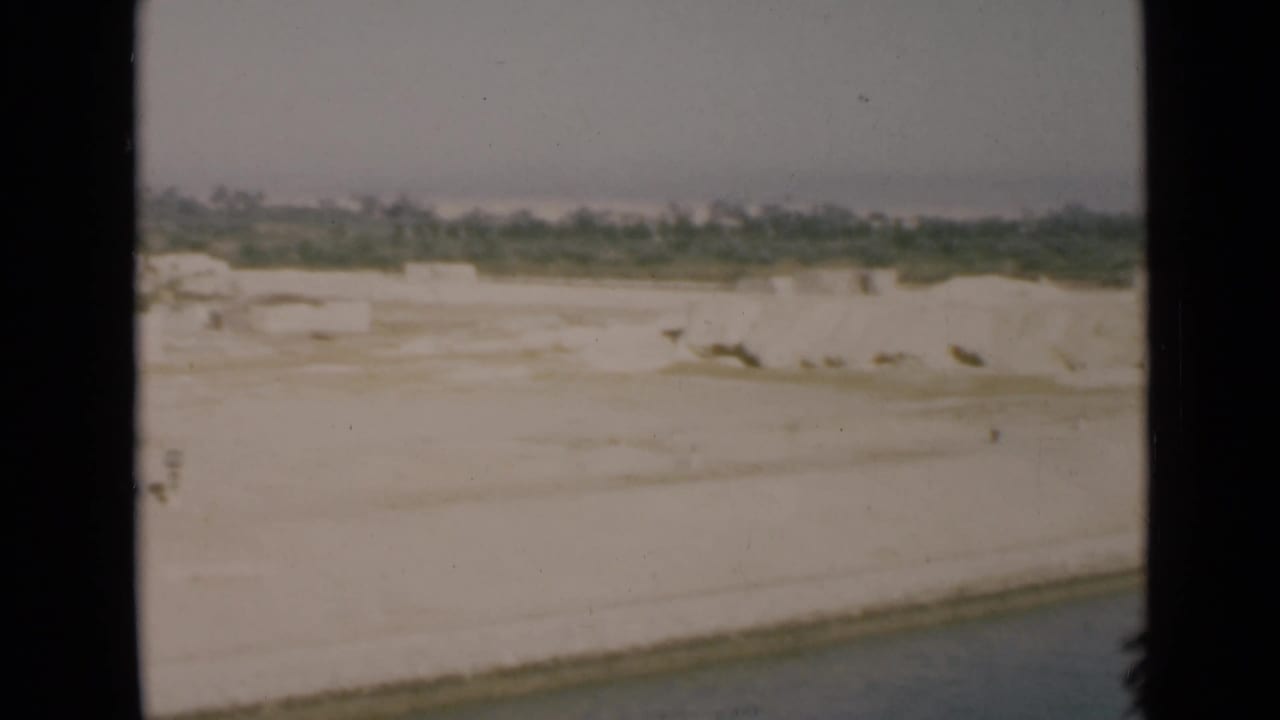 1946 Suez Canal view from a vessel showing a white sandy bank, calm water edge, and distant low greenery.
