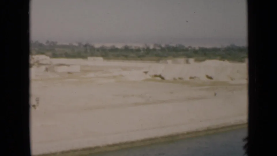 1946 Suez Canal view from a vessel showing a white sandy bank, calm water edge, and distant low greenery.