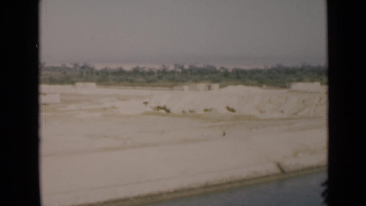 Shipboard 1946 Suez Canal view of a bright sandy bank, narrow water edge, and distant tree line.