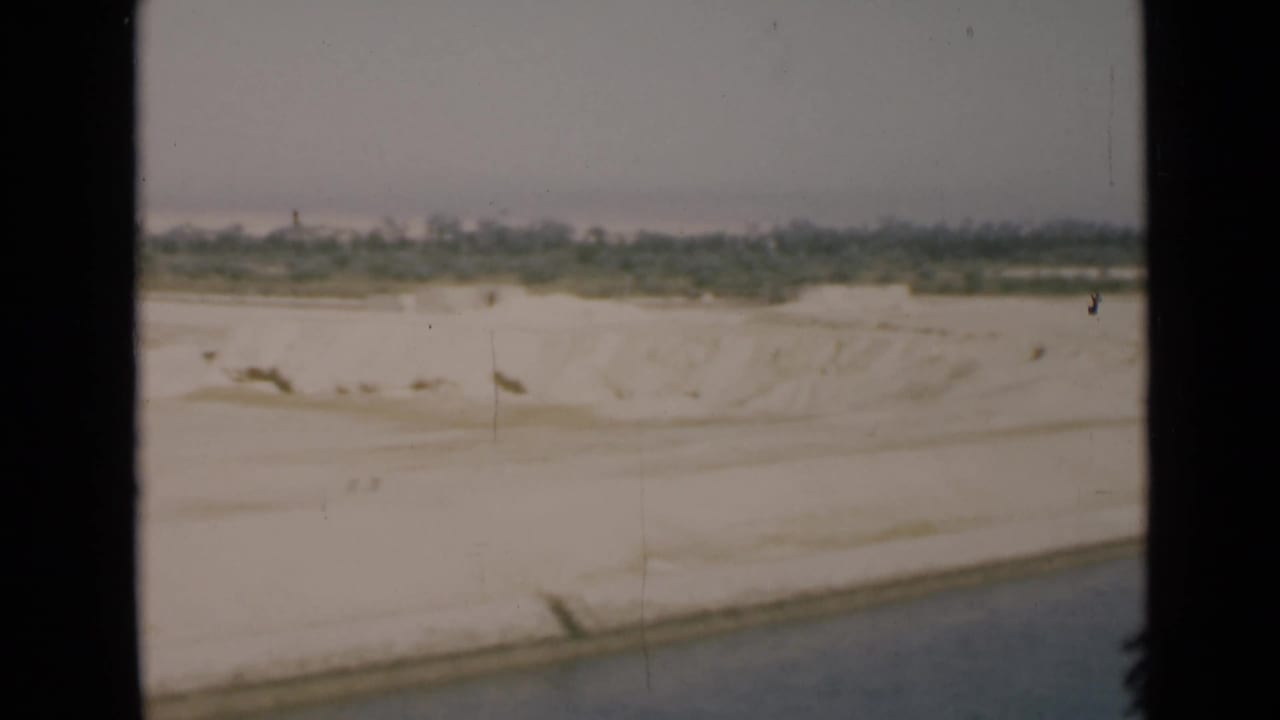 Sandy canal-side terrain with distant trees seen through dark frame edges.