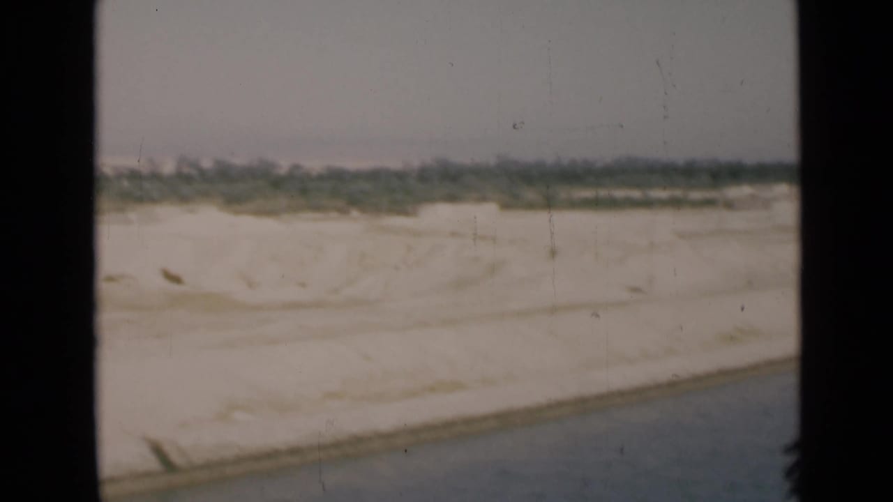 Wide sandy landscape with canal water at lower right and trees on the horizon.