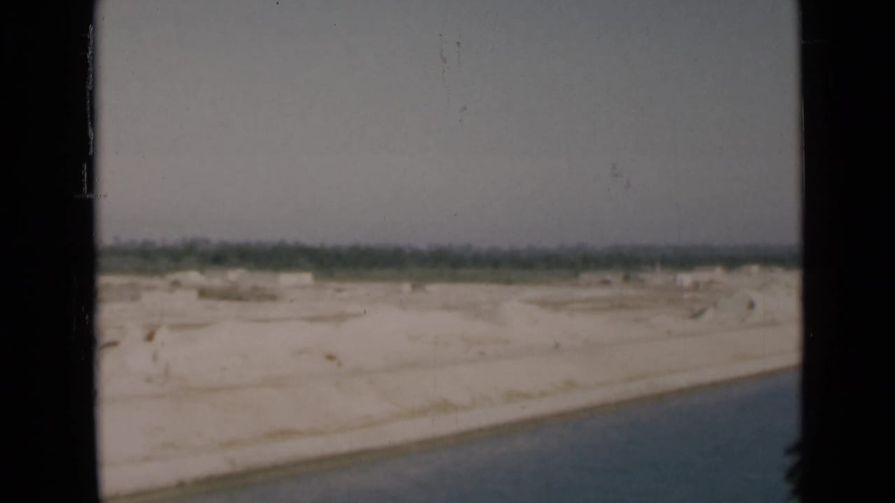1946 Egypt canal passage view with water in the foreground, pale sandy land, and distant trees beneath a muted sky.