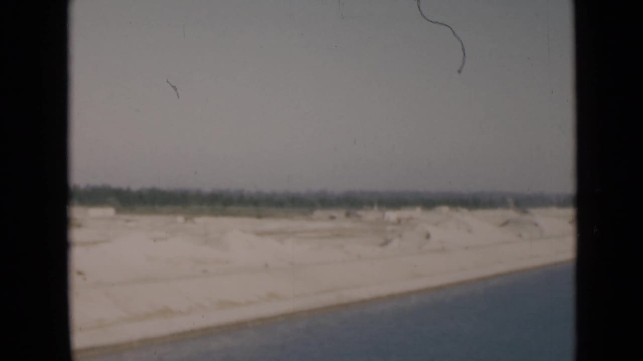 1946 Suez Canal view with a broad white sand bank, blue water at right, distant vegetation, and soft 8mm texture.