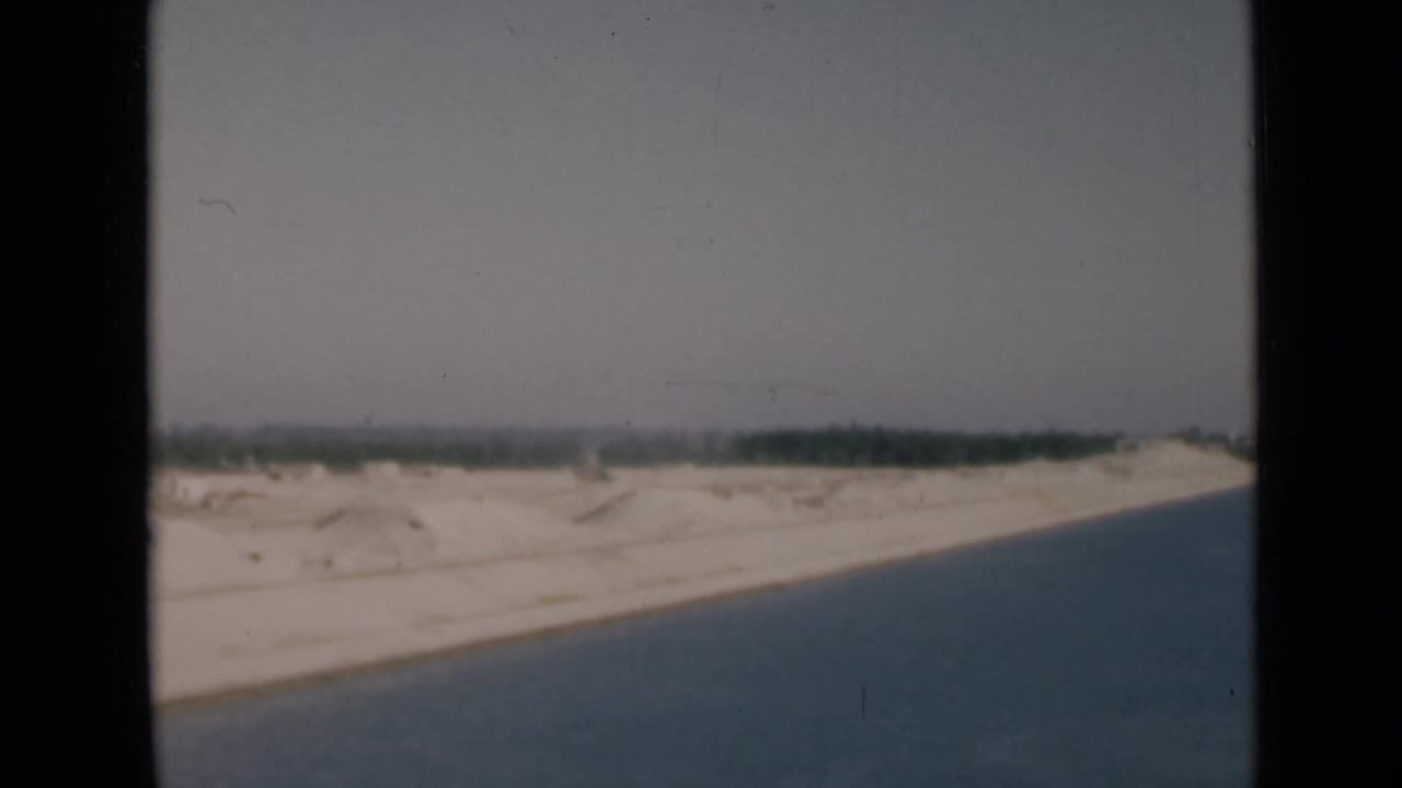 Soft 8mm 1946 Suez Canal frame showing a sloping sandy shore, blue canal water, and a dark green horizon line.