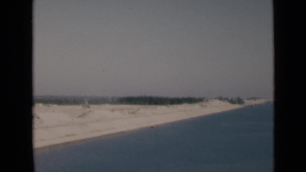 1946 8mm view of the Suez Canal area, with blue water running beside a pale sandy bank and distant low vegetation.