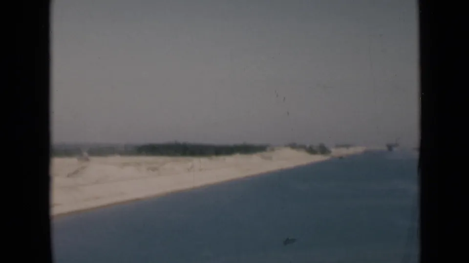 1946 Suez Canal home-movie frame showing calm blue water, pale sandy banks, and a faint distant shoreline.