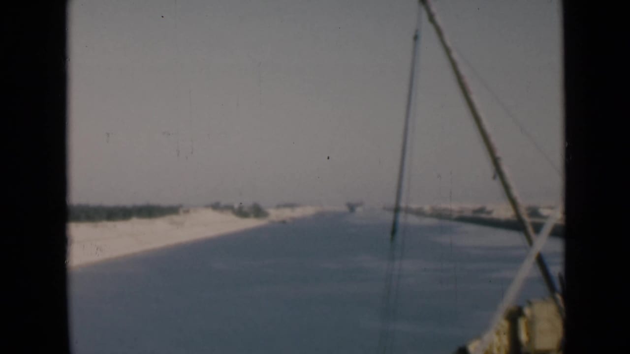 Canal water and sandy banks seen from a boat with rigging in the foreground.