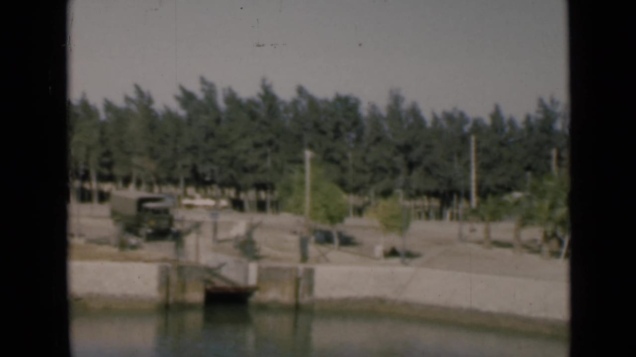 1946 Suez Canal view showing a small bridge or culvert, concrete banks, a dark truck, trees, and utility poles along the roadside.