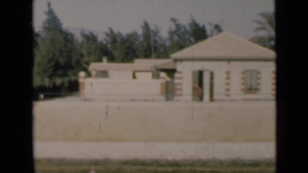 1946 Suez Canal home-movie frame showing a small pale building, shuttered windows, a wide yard, and trees.