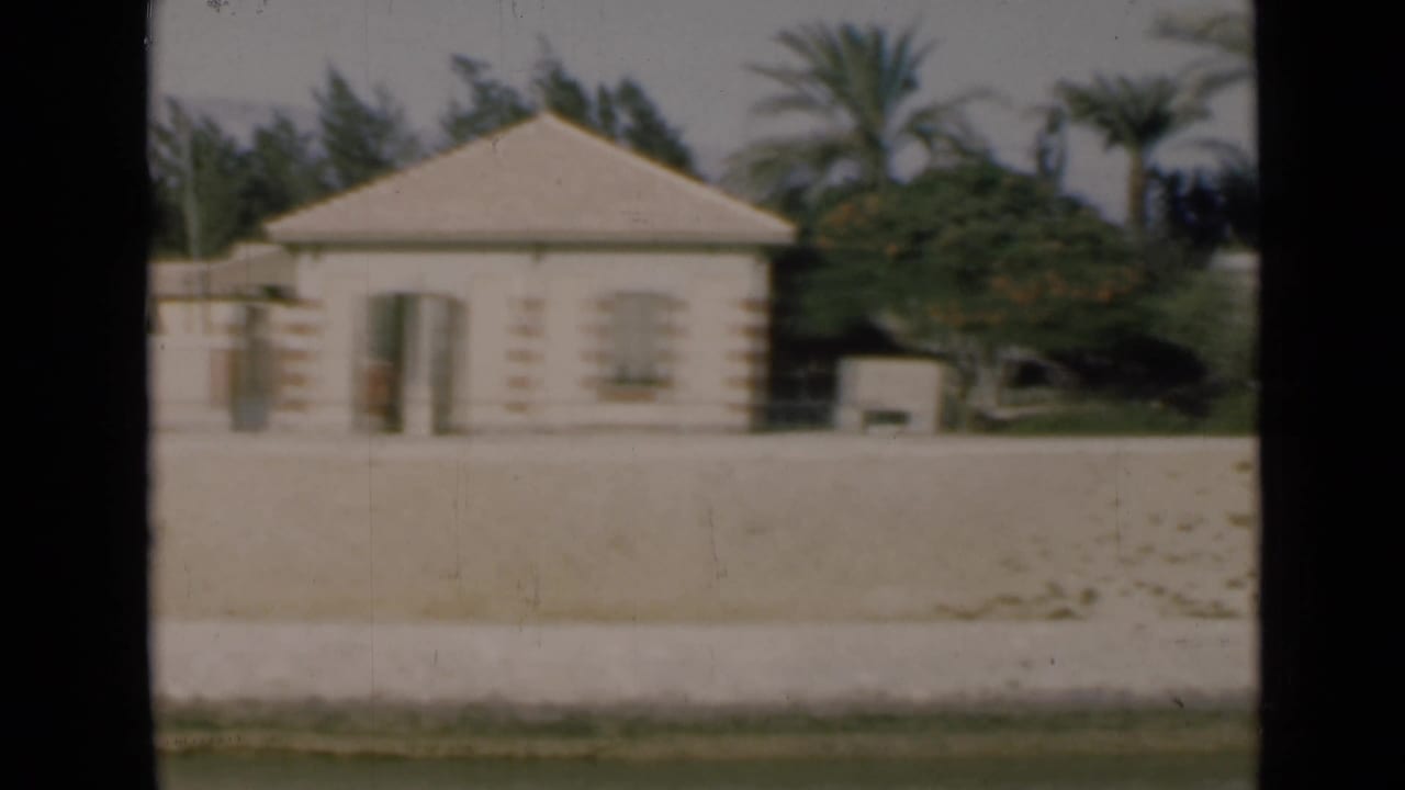 1946 Suez Canal frame showing a pale house with a low roof, palms, trees, and a broad sandy foreground.